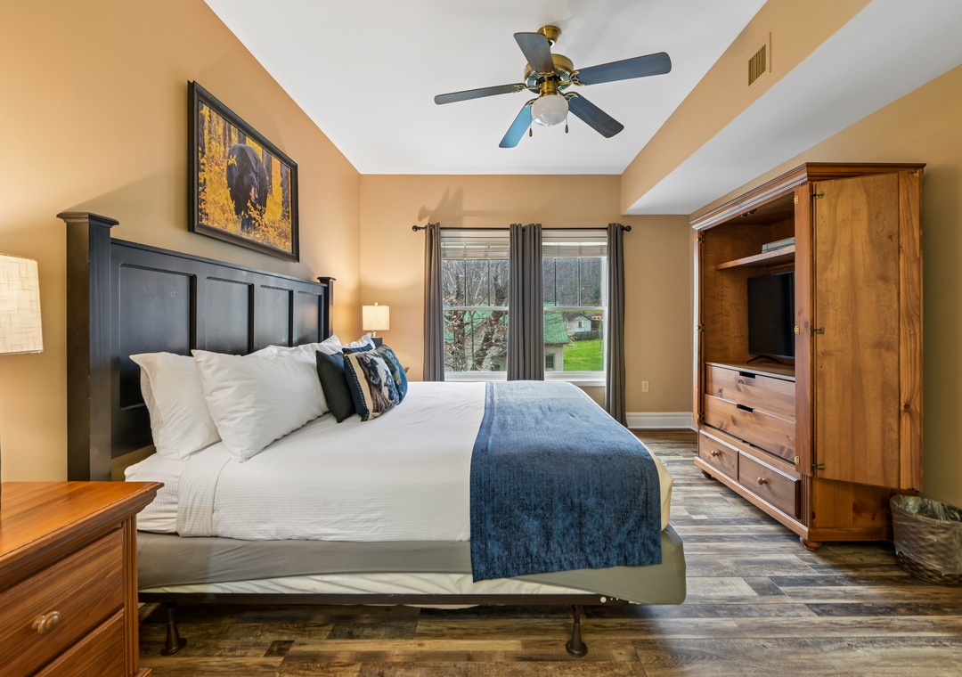 Unwind in your spacious bedroom featuring a plush king bed, elegant wood furnishings, and peaceful garden views from your private window.