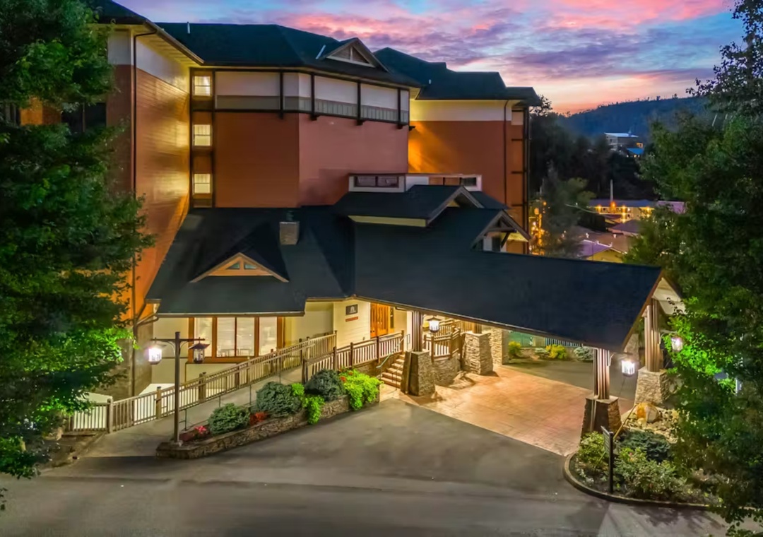 A stunning mountain property illuminated against a vibrant sunset sky, surrounded by lush forests and nestled in a peaceful hillside setting.