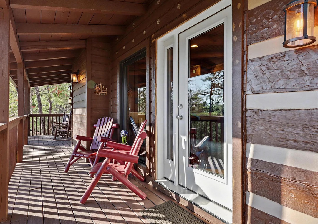 Charming covered porch with rustic wood beams and colorful Adirondack chairs, inviting you to relax with your morning coffee while soaking in peaceful woodland views.