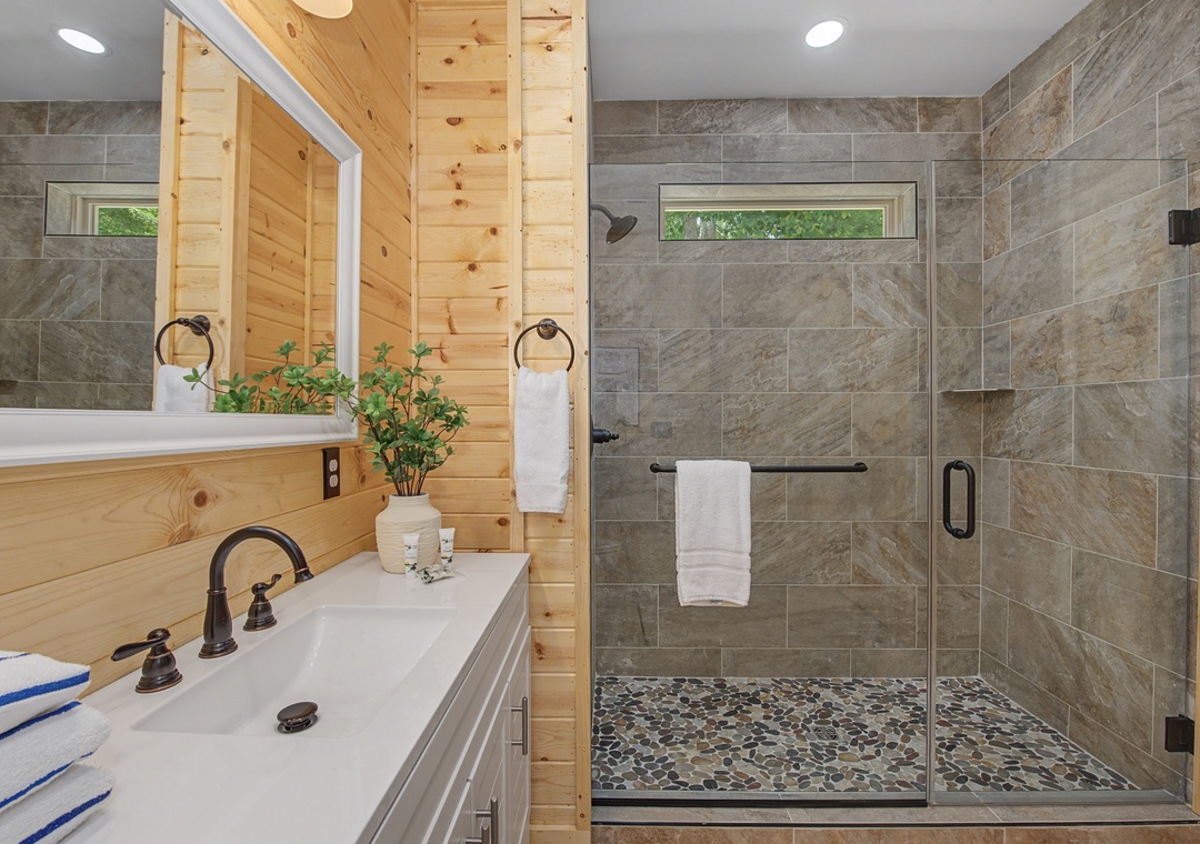 Your private bathroom blends natural wood warmth with modern tile and a spacious walk-in shower. Plush towels and a peaceful view through the shower window await you.
