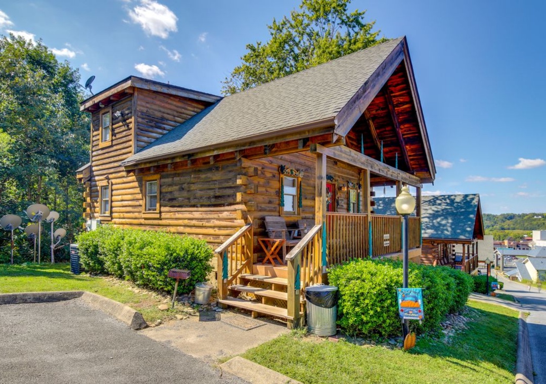 A charming log cabin with covered porch and wooden stairs, nestled among mature trees in a peaceful residential setting.