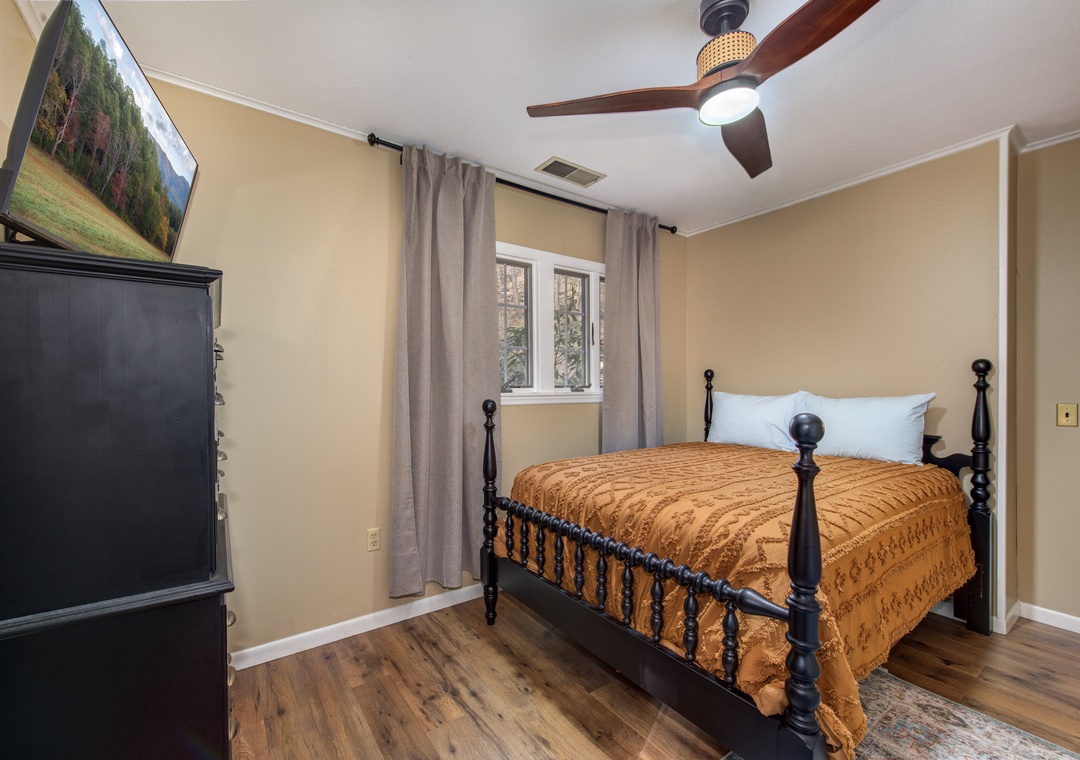 Unwind in your cozy bedroom featuring a classic spindle bed, entertainment setup, and ceiling fan for perfect comfort.