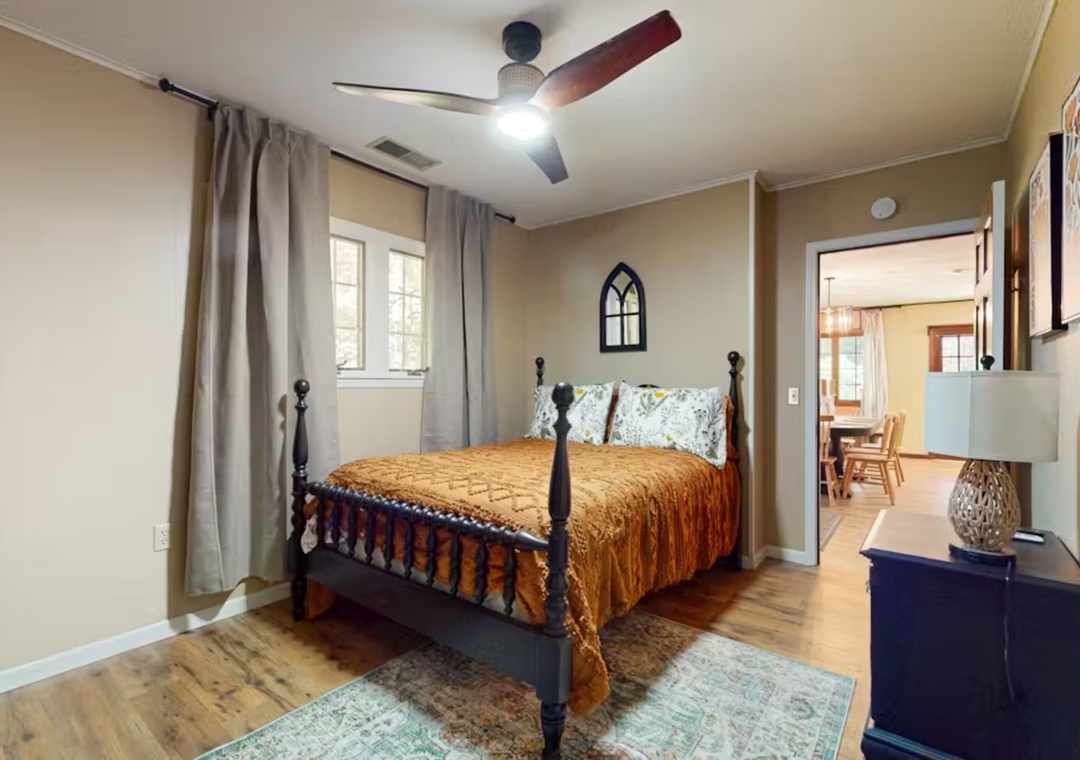 Rest in your charming bedroom featuring a classic four-poster bed, warm wood floors, and gentle natural light filtering through soft curtains.