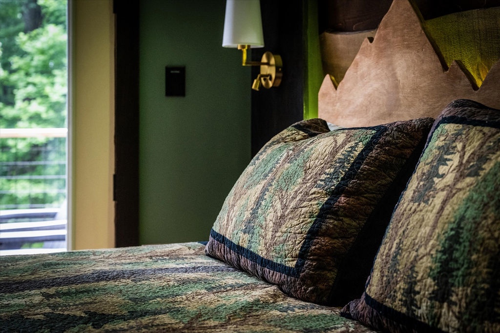 Sink into these plush quilted pillows and let the soft glow of the brass sconce light your evening. Your serene retreat awaits, framed by garden views just beyond the window.