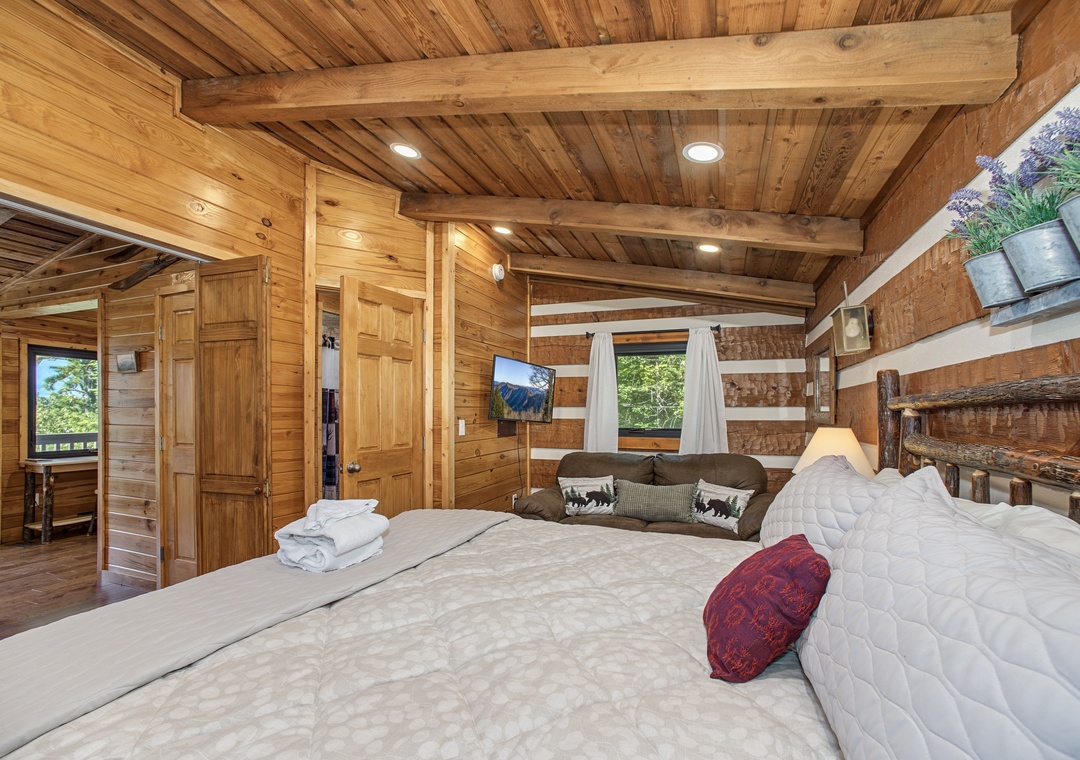 Wake up surrounded by warm natural wood and rustic elegance. Your spacious bedroom features vaulted ceilings, charming beam details, and natural light streaming in from multiple windows—a perfect mountain retreat.