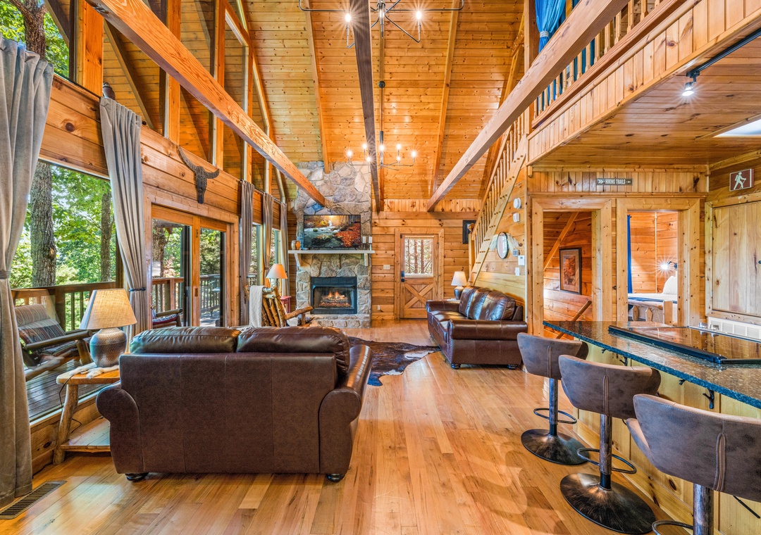 Relax in the warmth of your private cabin's soaring great room, where rich wood beams frame plush leather seating and a stone fireplace anchors cozy evenings together.