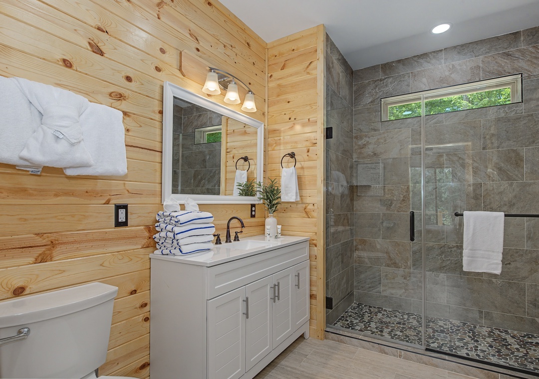 Your private bathroom features a sleek walk-in shower with pebble flooring, modern tile work, and a bright vanity with fresh towels—a serene spot to refresh after a day of exploring.