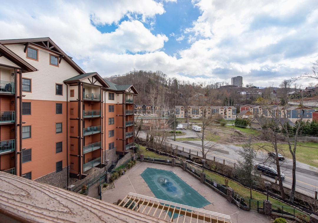 Multi-story residential complex featuring modern apartment buildings, a community swimming pool, and scenic views of surrounding neighborhoods and distant cityscape.