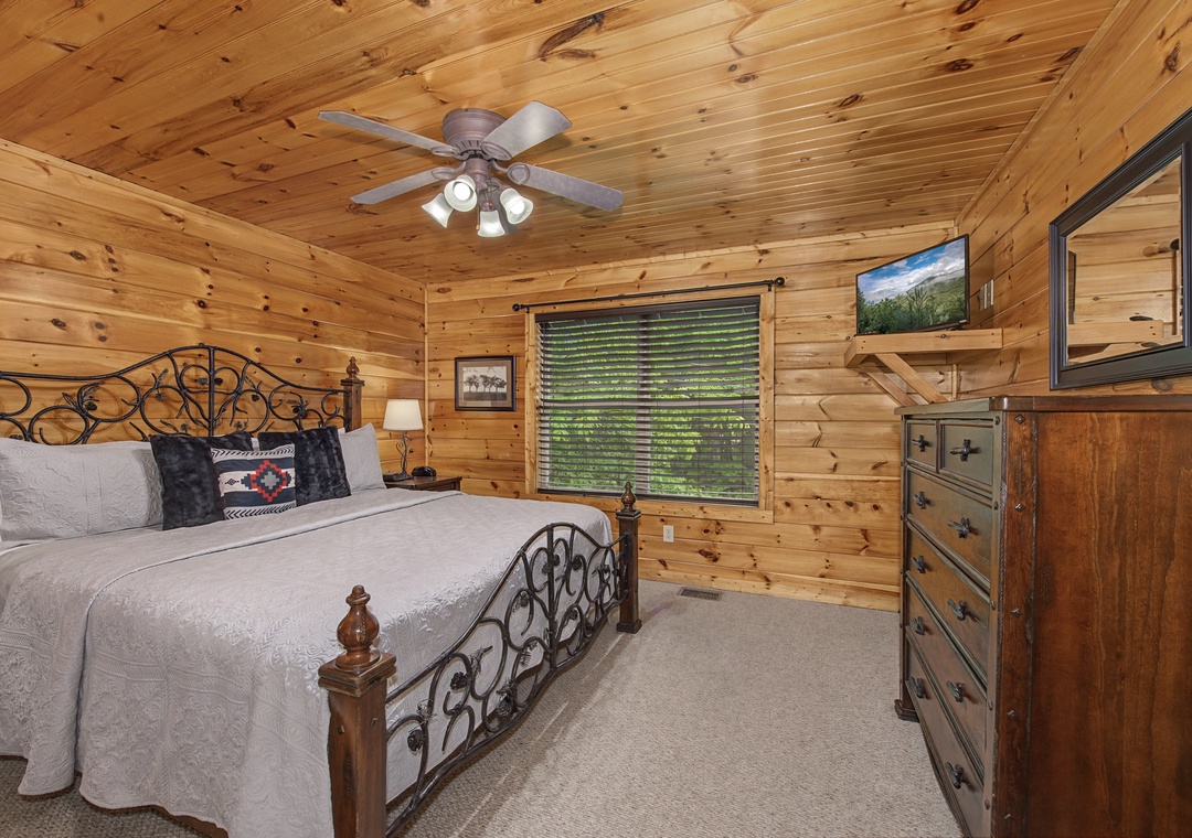 Drift off under the gentle whirl of the ceiling fan in this cozy cabin bedroom with rich wood paneling and mountain views from your window.