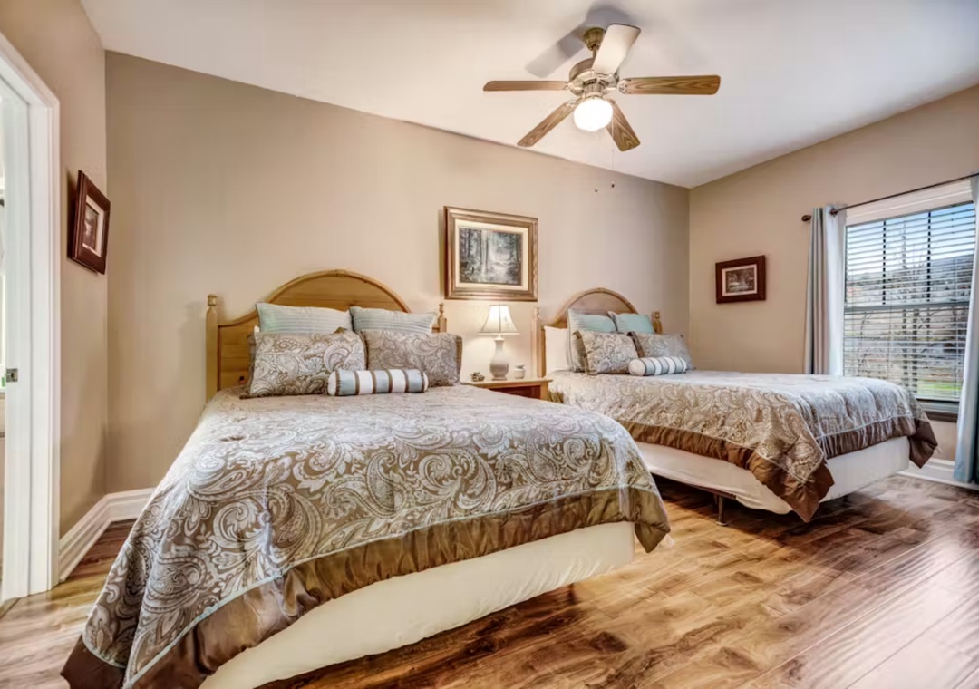 Your comfortable bedroom features two cozy beds with elegant linens, warm hardwood floors, and a ceiling fan for perfect temperature control.