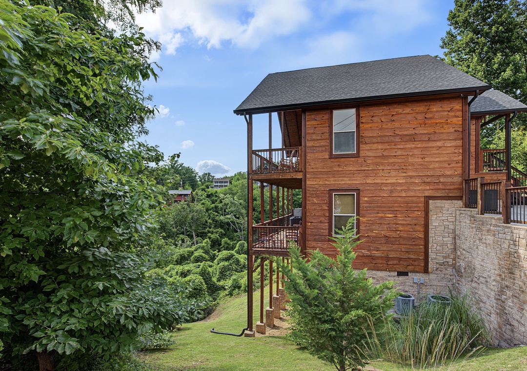 A charming wooden cabin nestled among lush trees, featuring multi-level balconies and scenic mountain views, offering a peaceful retreat surrounded by natural beauty.