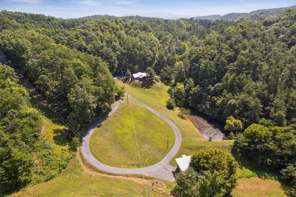 Aerial view of the property nestled within lush forested hills, accessed by a winding private drive through vibrant natural surroundings.
