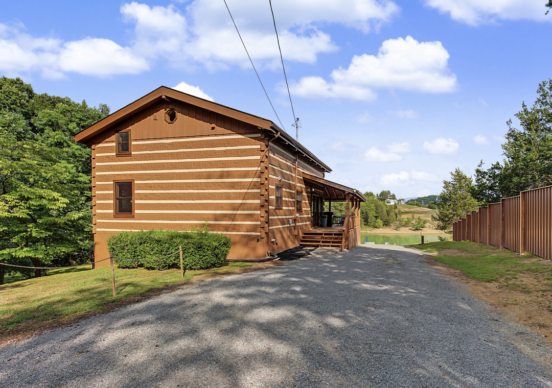 Charming log cabin with spacious parking nestled among lush greenery and rolling hills, offering a peaceful countryside retreat under bright skies.