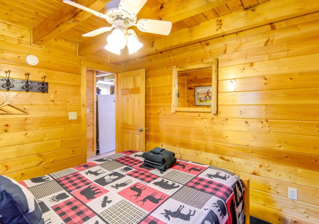 Your cozy log cabin bedroom features warm wood walls, ceiling fan, and rustic plaid bedding for mountain retreat vibes.
