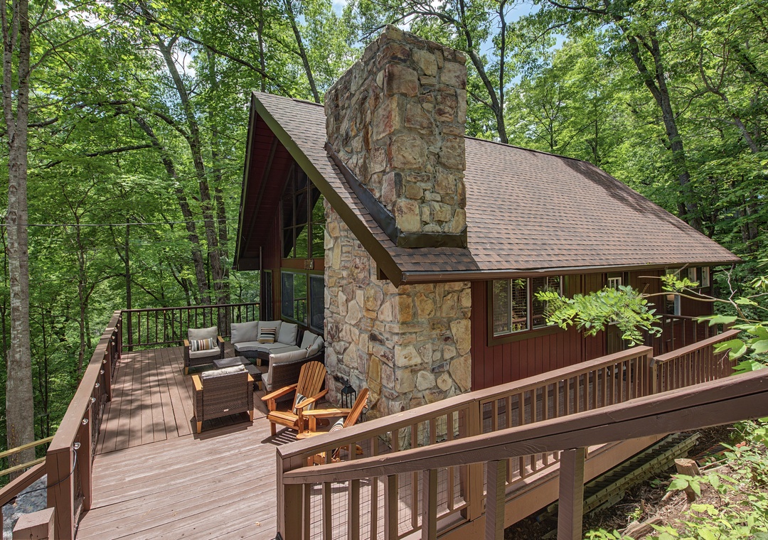A charming cabin nestled in lush woods with a stone fireplace and wraparound deck featuring cozy seating where you can unwind and soak in serene forest views.
