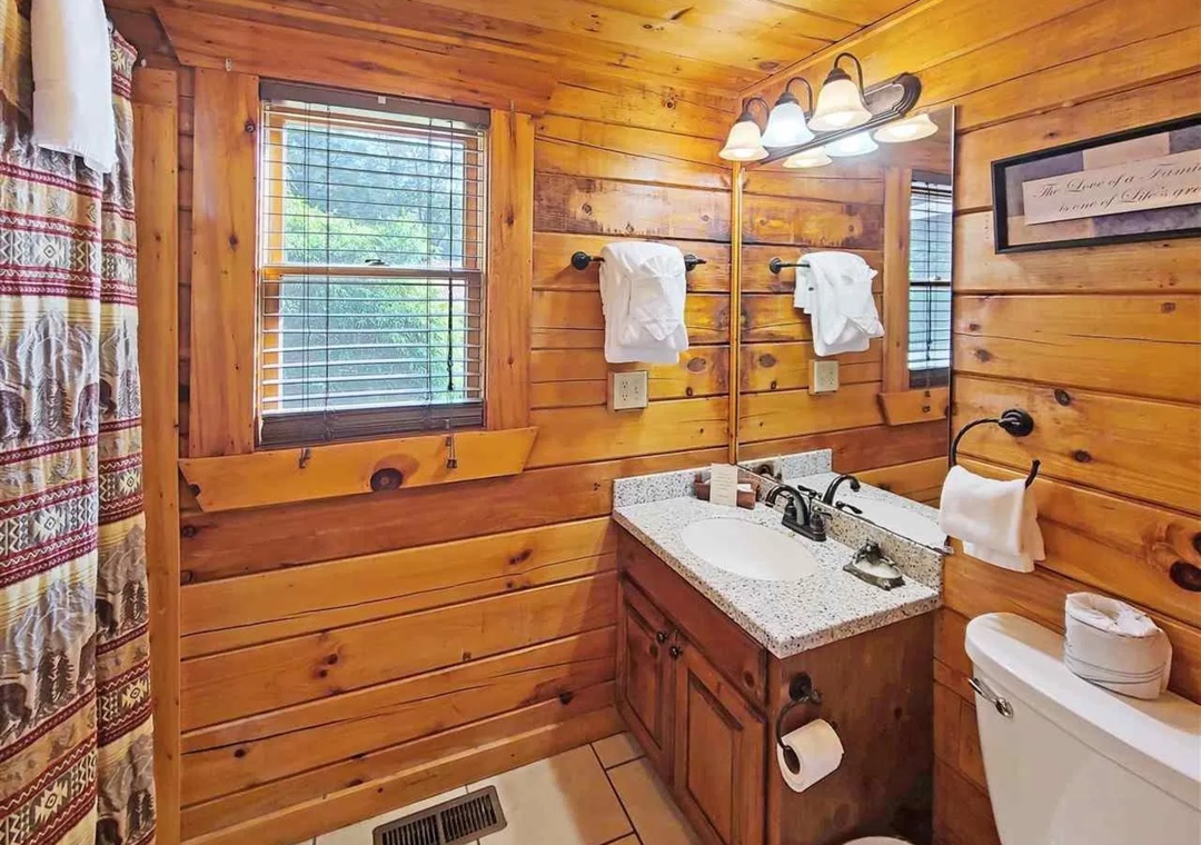 Step into your rustic cabin bathroom with warm log walls, granite counters, and plush towels waiting for your arrival.