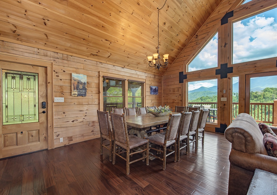 Gather around this rustic dining table with mountain views framing your meals. The soaring wood-beamed ceiling and floor-to-ceiling windows invite natural light and stunning scenery into your shared moments.