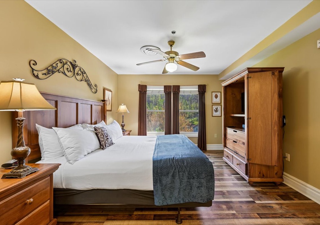 Unwind in your elegant bedroom featuring a plush king bed, warm wood furnishings, and peaceful natural views from your window.
