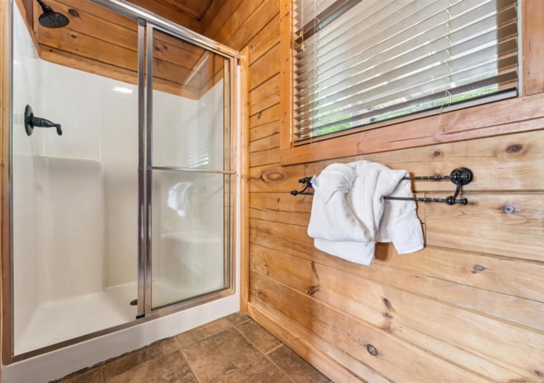 Step into your private rustic bathroom, where warm wood walls and a sparkling clean shower await. Plush towels hang ready for you, blending cabin charm with modern comfort.
