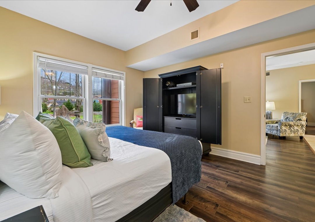 Relax in your spacious bedroom featuring exposed ceiling beams, elegant hardwood floors, and a wall-mounted TV for cozy evening entertainment.