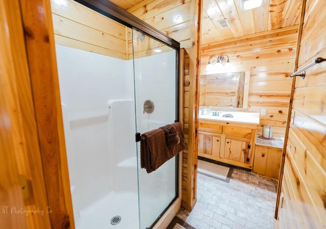 Step into your private bathroom, where rustic wood walls meet modern comfort. A spacious glass-enclosed shower awaits, with fresh towels at hand and a charming vanity ready for your morning routine.