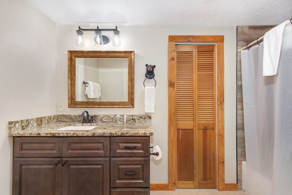Your rustic bathroom features a granite-topped vanity, framed mirror with vintage-style lighting, fresh white towels, and charming wood accents that blend comfort and mountain-lodge appeal.