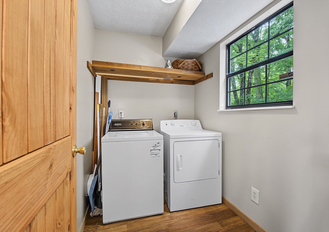 Natural light fills your private laundry area, where a full-size washer and dryer await. The woodland view through the window makes even chores feel peaceful.