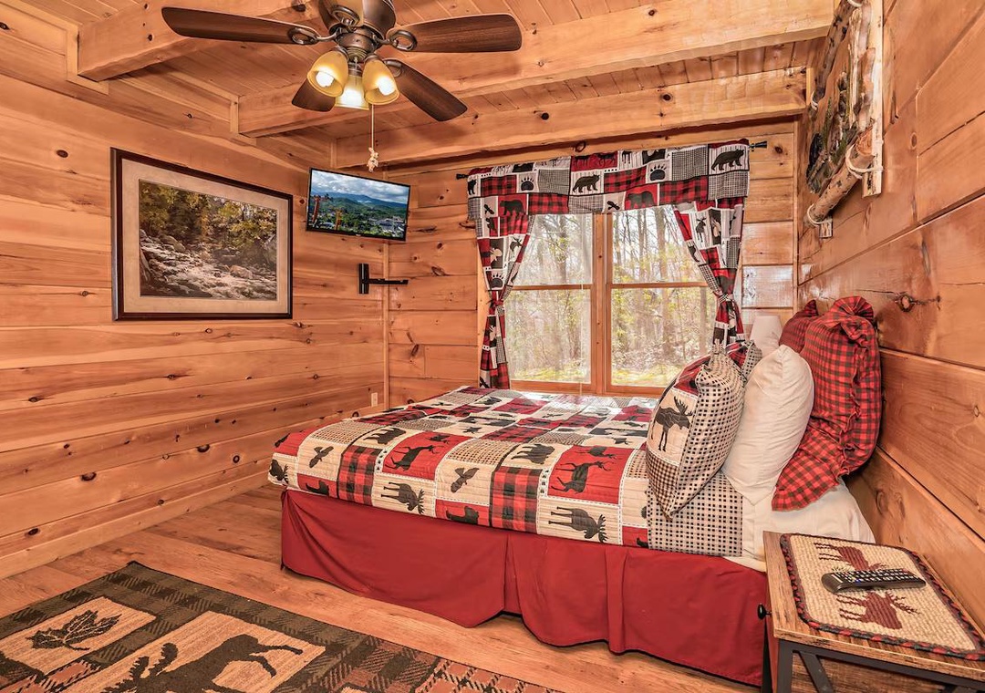 Cozy up in your rustic cabin bedroom with charming plaid bedding, warm wood walls, and a ceiling fan for comfort.