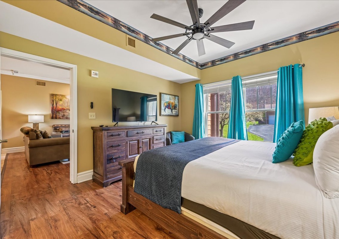 Unwind in your spacious bedroom with vibrant turquoise accents, comfortable queen bed, and peaceful garden views through large windows.