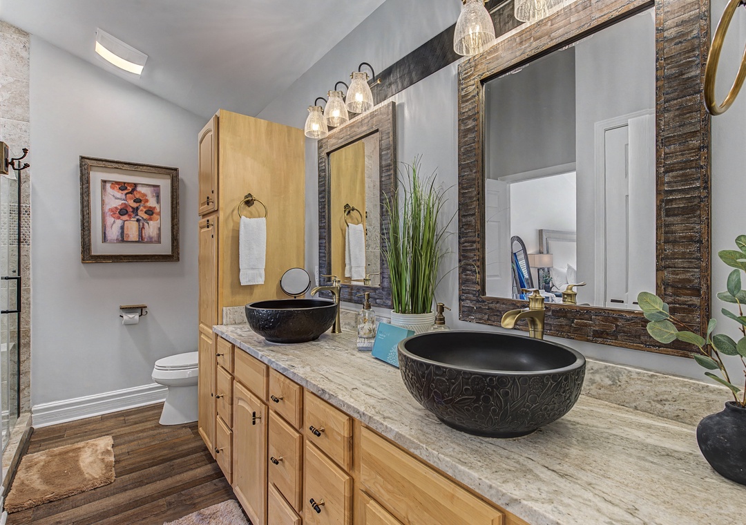 Indulge in this stunning master bathroom featuring dual vessel sinks, warm wood vanity, and rustic mirrors for your morning rituals.