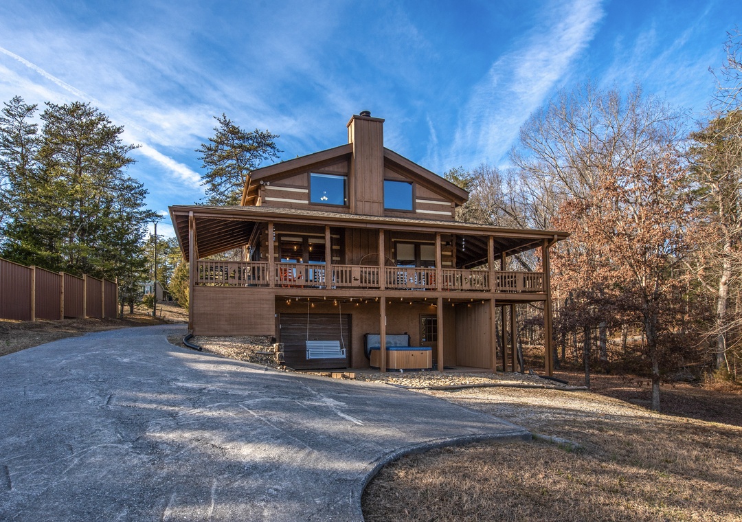 Rustic mountain cabin with wraparound deck and hot tub, surrounded by peaceful woodland setting.
