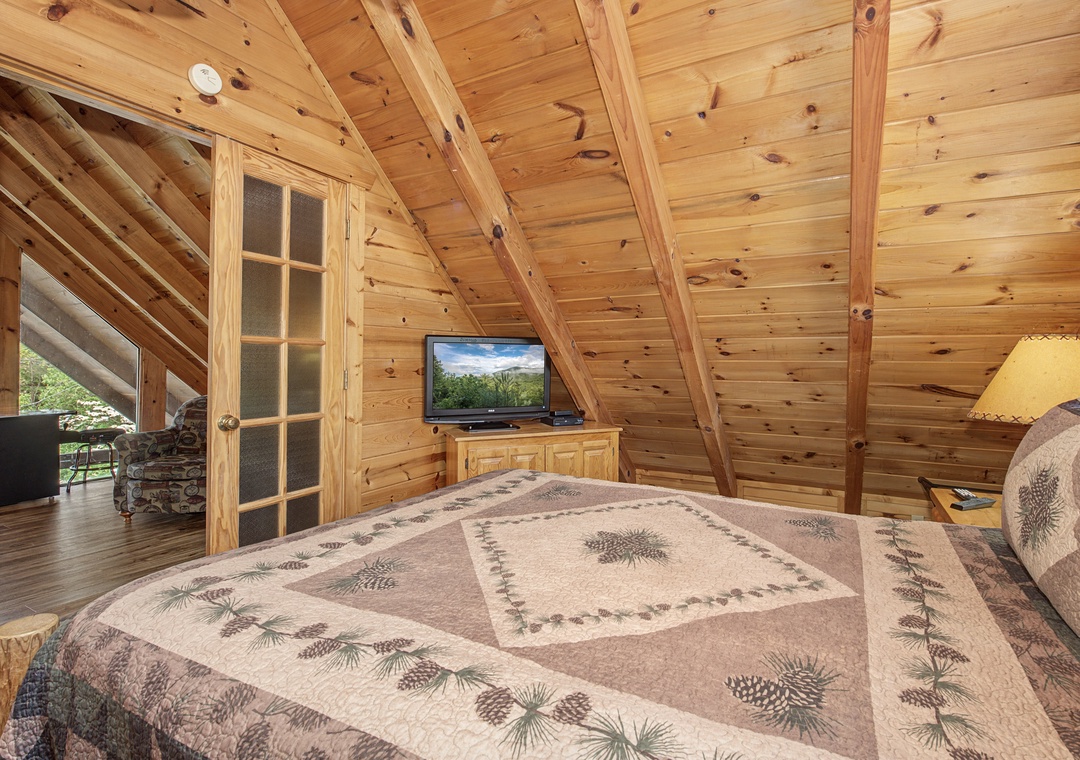 Drift off surrounded by rustic pine walls and beams in your cozy loft bedroom, complete with flat-screen TV for relaxing evenings.