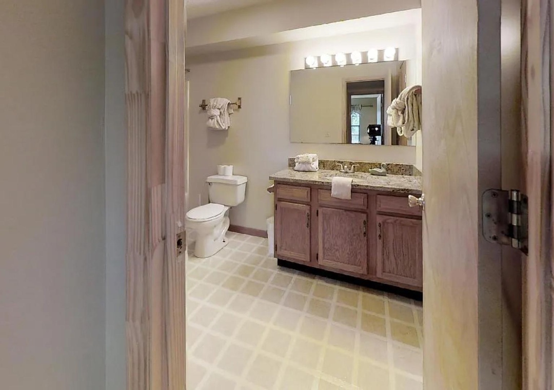 Your private bathroom features a spacious vanity with granite countertops, warm wood cabinetry, and bright Hollywood-style lighting to make every morning feel special.