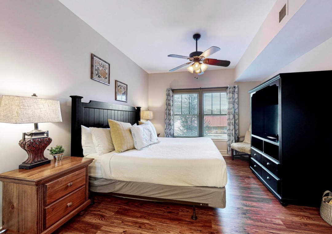 Sink into plush bedding in your elegant master bedroom, featuring rich hardwood floors and modern entertainment center.