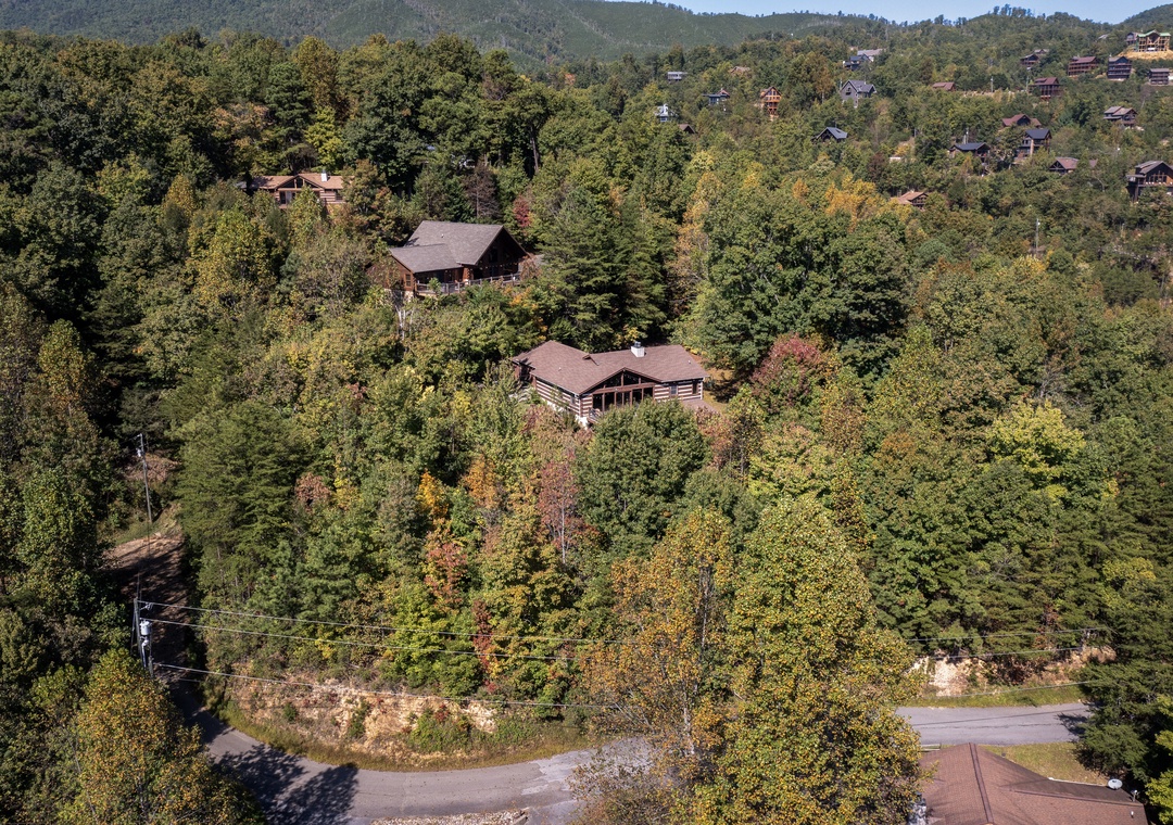 Aerial view capturing two rustic cabins nestled among vibrant autumn foliage in a peaceful mountain neighborhood, offering a secluded retreat surrounded by nature's seasonal beauty.