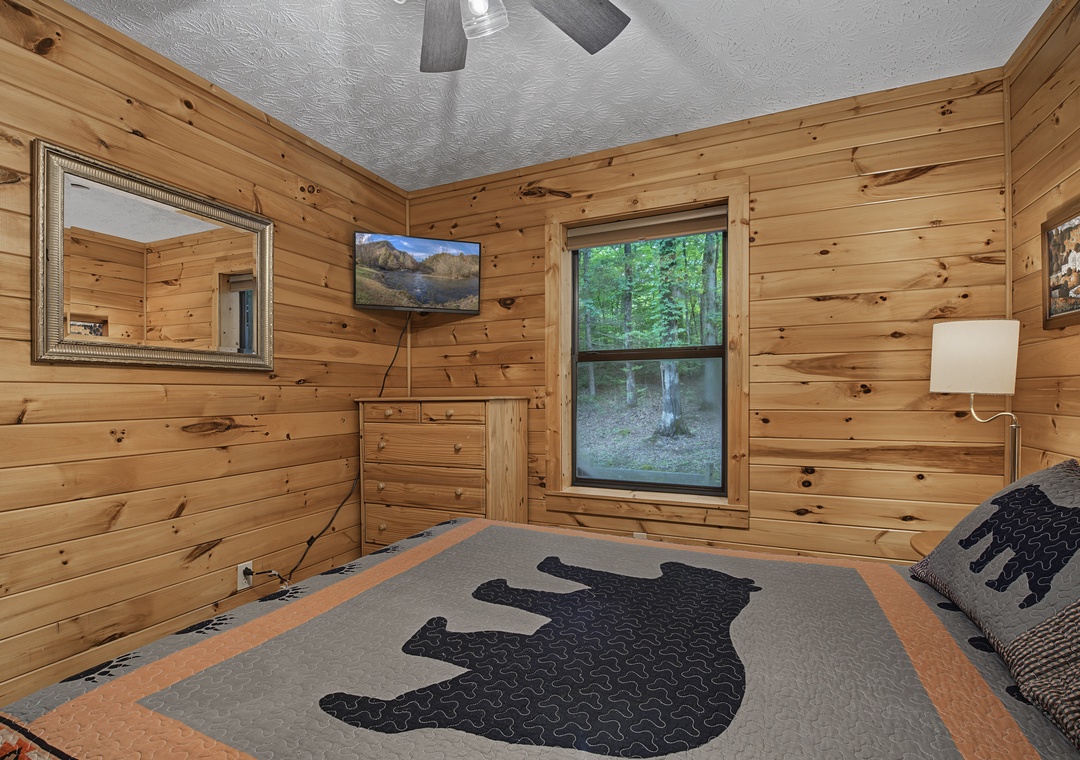 Rustic wood paneling frames your restful escape, where the ceiling fan hums gently, and tree-filled views greet you each morning through the window.
