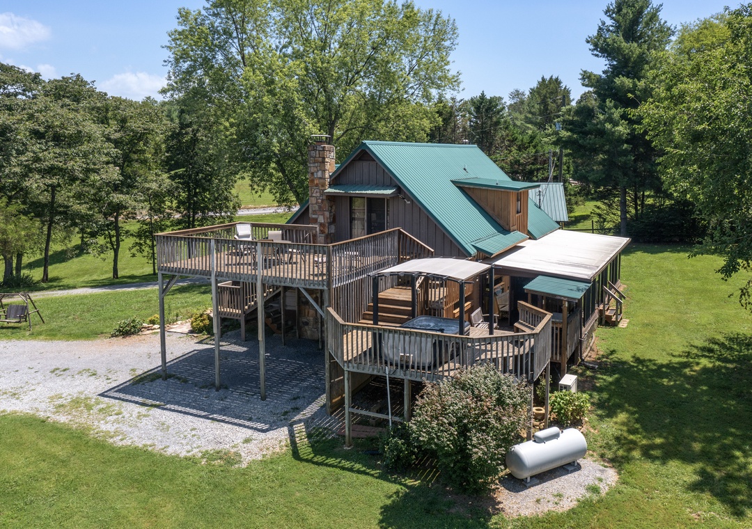 A secluded cabin with distinctive green roof nestled among mature trees on spacious grounds, offering peaceful woodland surroundings and multiple outdoor deck levels for relaxation.