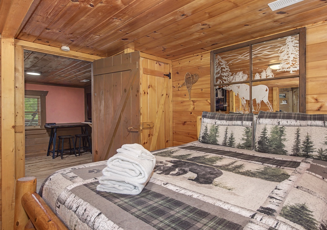 Cozy wood-paneled bedroom with wilderness-themed bedding where you'll drift off surrounded by rustic charm and mountain lodge ambiance.