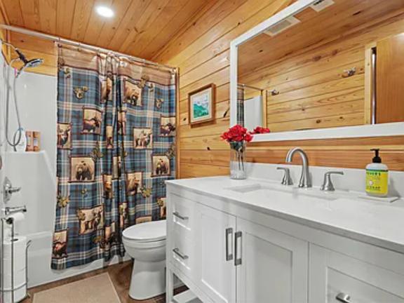 Step into your cabin-style bathroom with warm wood walls, a crisp white vanity, and a charming rustic-themed shower curtain. Fresh flowers and modern fixtures make it feel cozy yet refined.