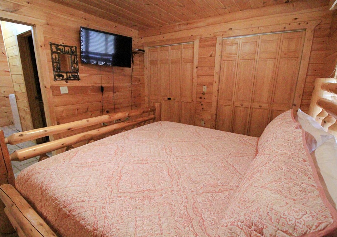 Cozy up in your rustic wood-paneled bedroom featuring a comfortable bed and mounted TV for relaxing evenings after your mountain adventures.