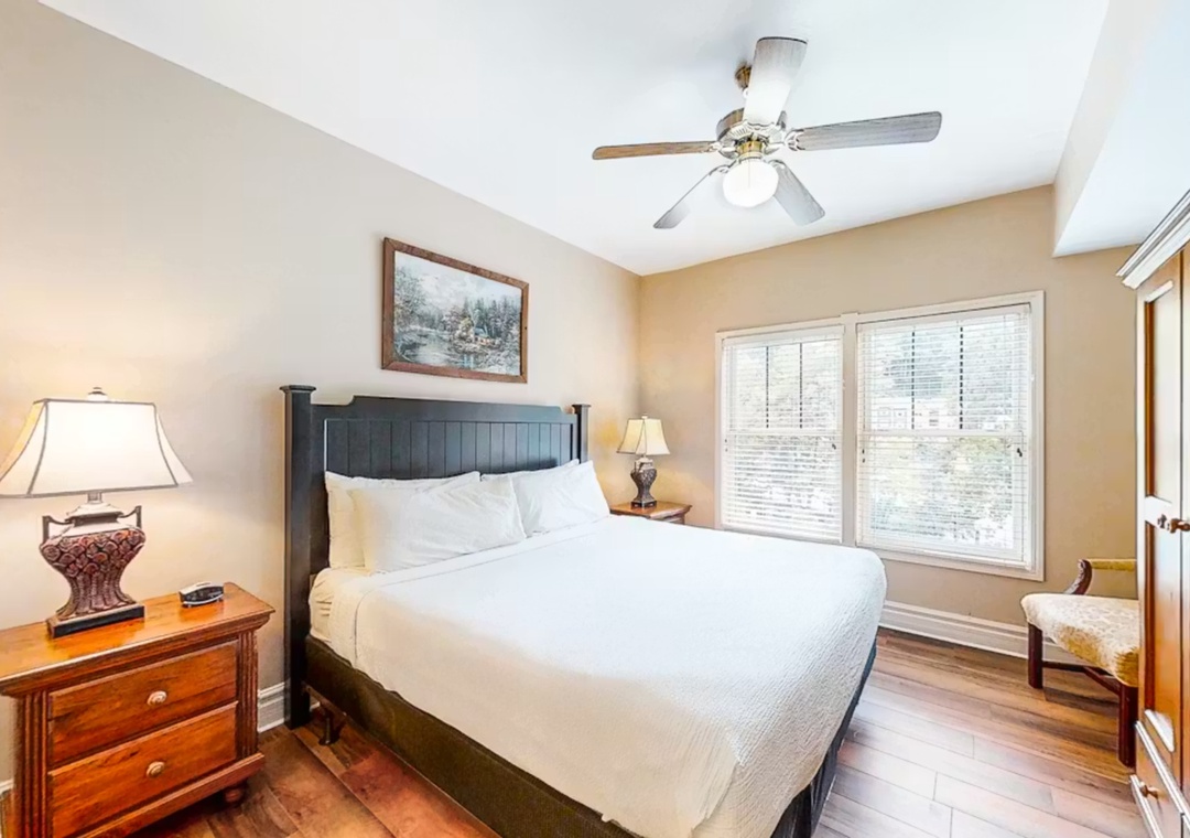 Sink into crisp white linens in your peaceful bedroom retreat, where warm wood floors and gentle ceiling fan create perfect sleeping comfort.