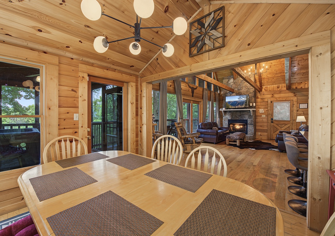 Gather around the dining table for meals while enjoying natural light and views of the surrounding greenery. The open layout connects seamlessly to the cozy living area with its stone fireplace.