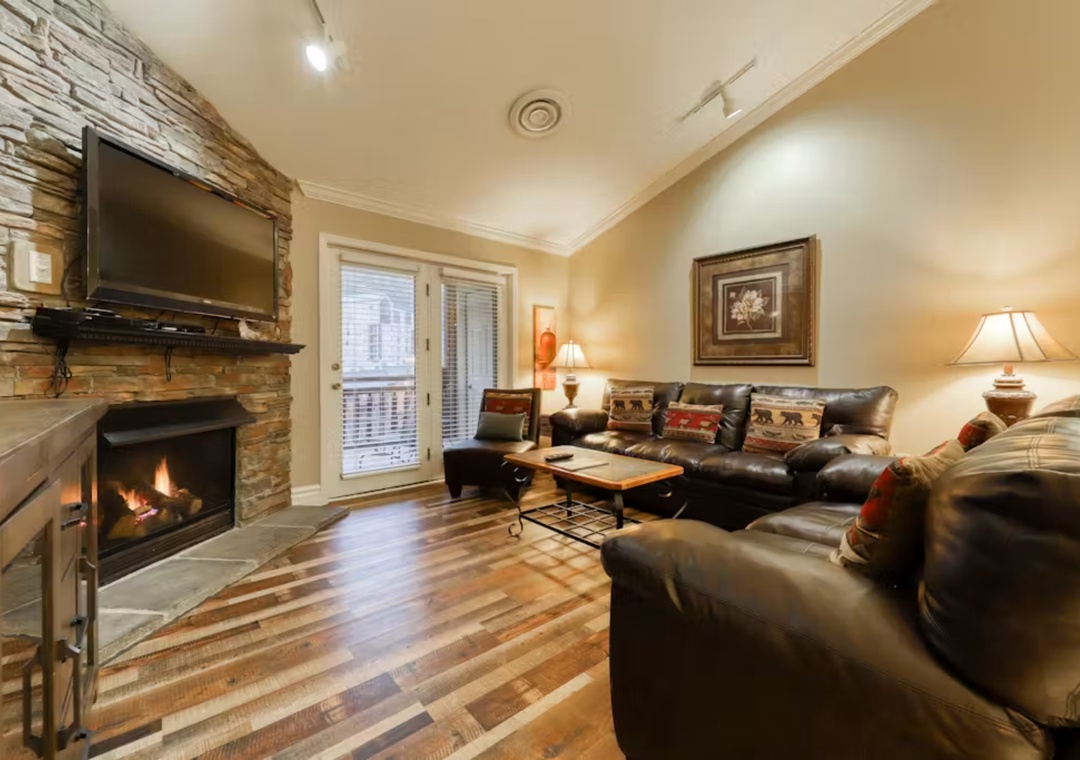 Relax in your cozy living room with crackling fireplace, leather seating, and warm mountain lodge ambiance perfect for unwinding.