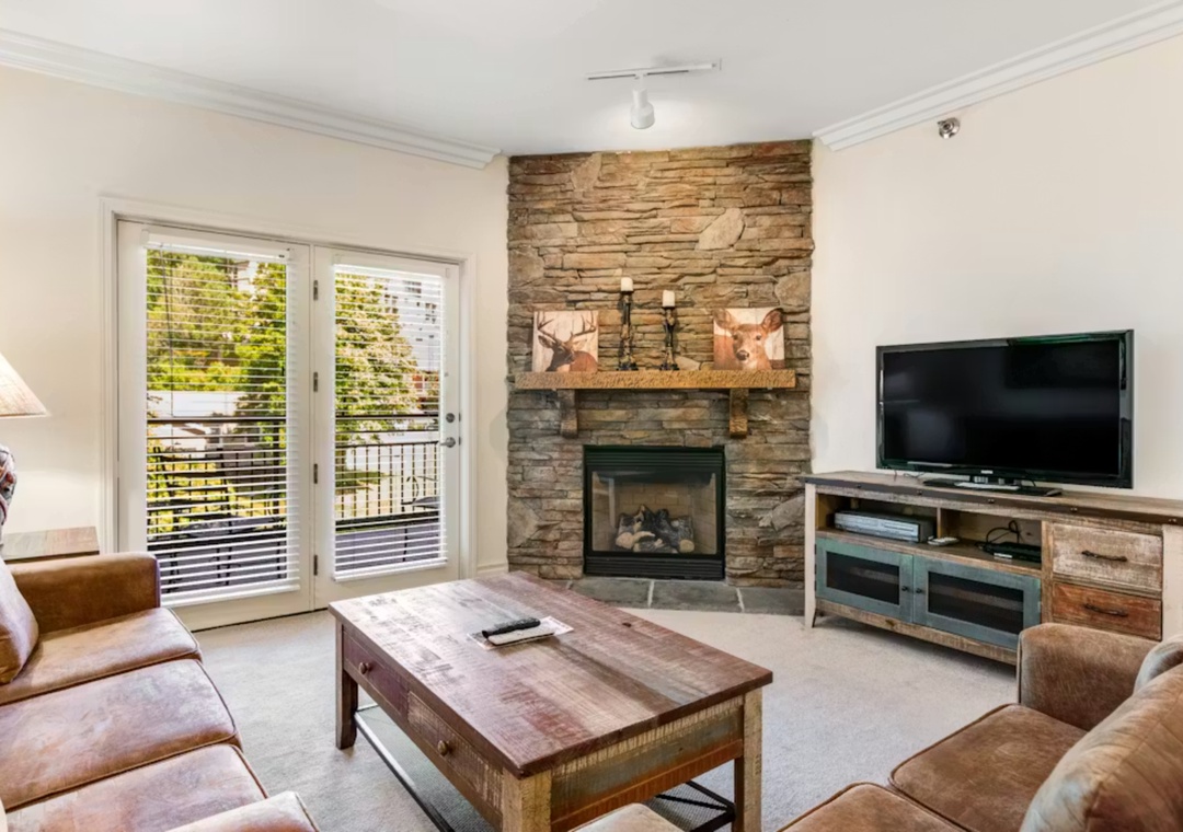 Cozy up in your rustic living room with stone fireplace, plush seating, and balcony access for mountain retreat vibes.