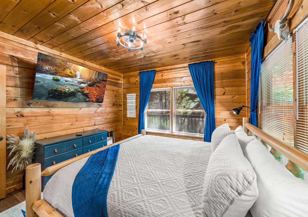 Sink into this plush bed surrounded by warm pine walls and vibrant blue accents. You'll drift off under the rustic chandelier and wake to natural light streaming through large windows.