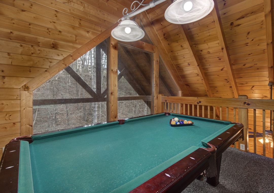 Challenge friends to pool in this cozy loft game room, where rustic wood beams frame forest views beyond the felt.