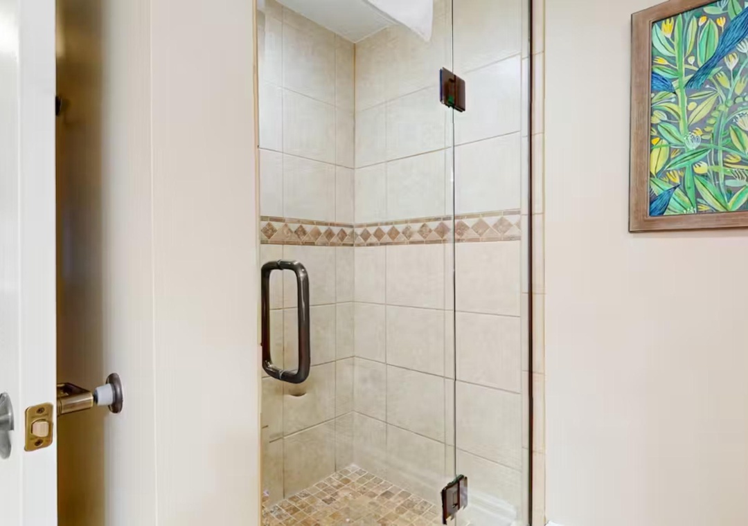 Step into your private glass-enclosed shower with beautiful tile accents and tropical artwork—your personal spa awaits.