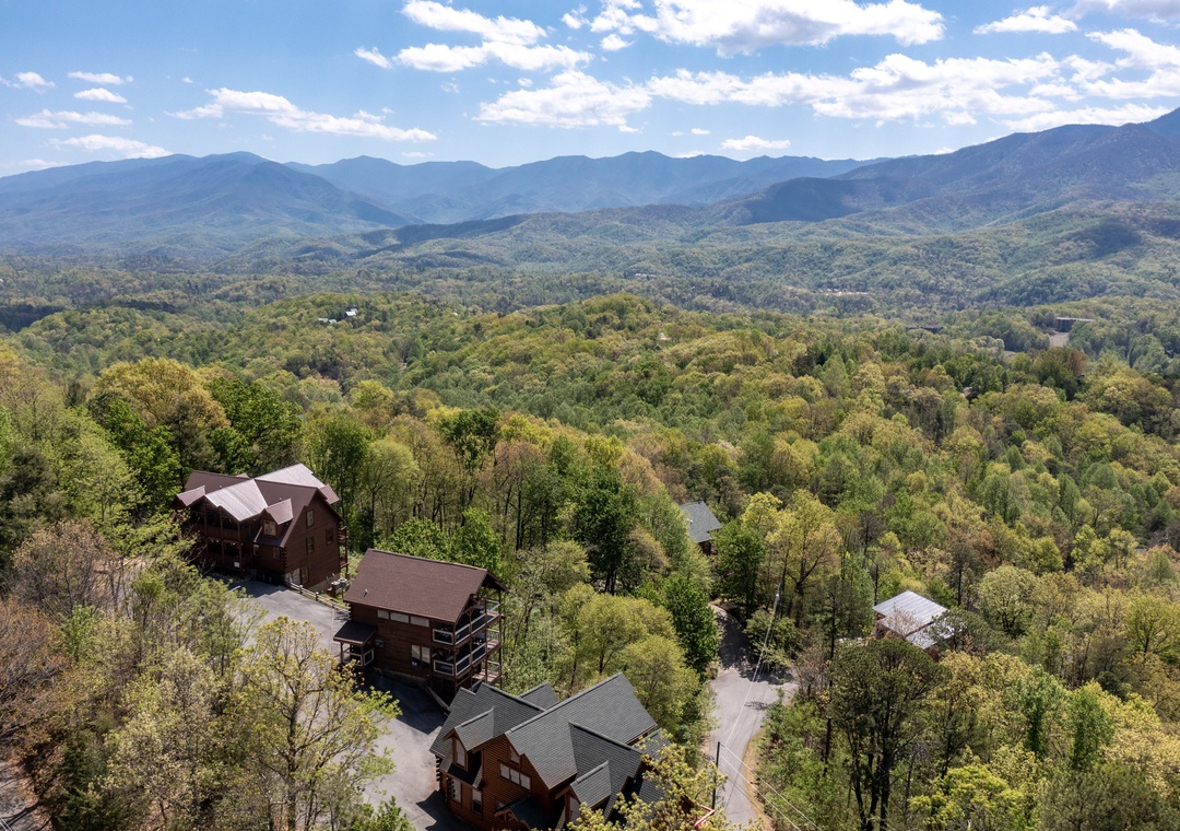Stunning aerial view reveals mountain cabin retreat nestled among rolling forested hills with majestic Blue Ridge peaks stretching endlessly beyond.