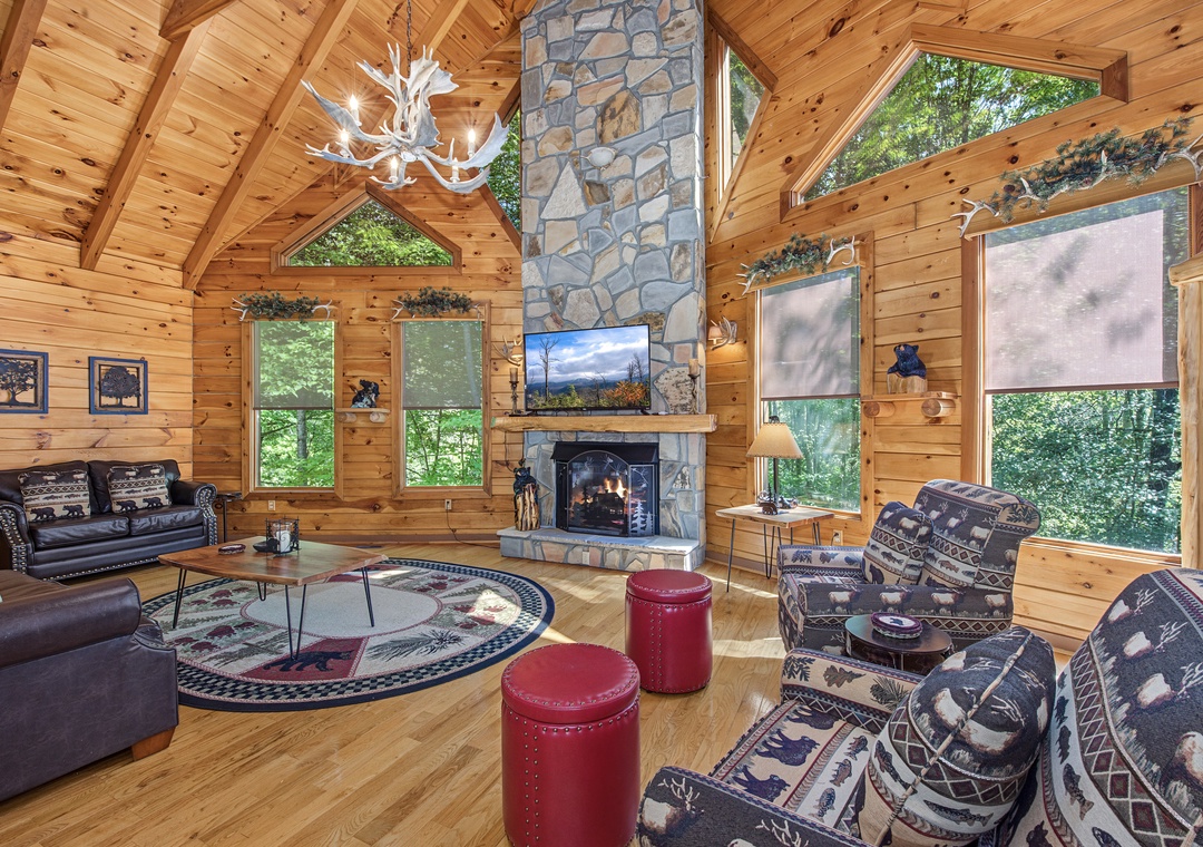 Gather around the cozy stone fireplace in this stunning great room, where soaring ceilings, warm wood paneling, and natural light create your perfect mountain retreat.