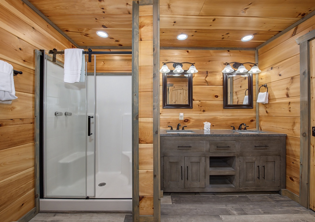 Step into your private bathroom with warm wood-paneled walls, a spacious walk-in shower, and a stylish double vanity—perfect for relaxing after a day of adventure.